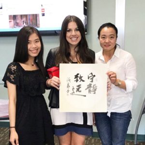 Three women holding a painting with Chinese characters